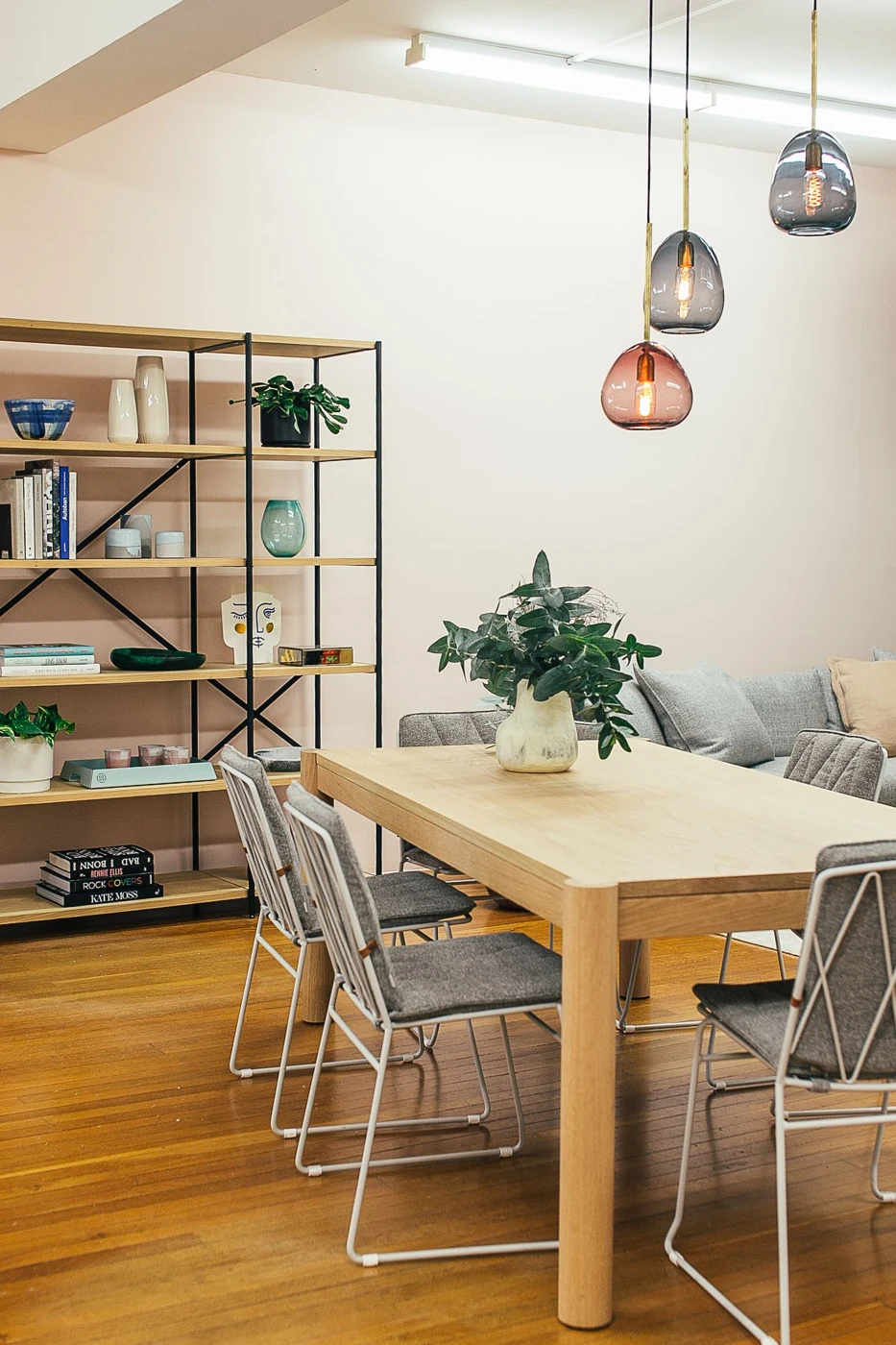 A bright living room with a wooden table, chairs, shelving and pale walls.
