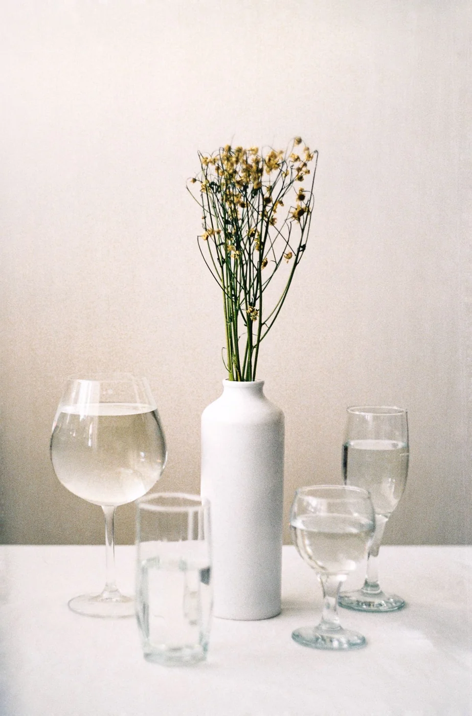 Minimalist still life featuring a white ceramic vase and glassware on a white background.