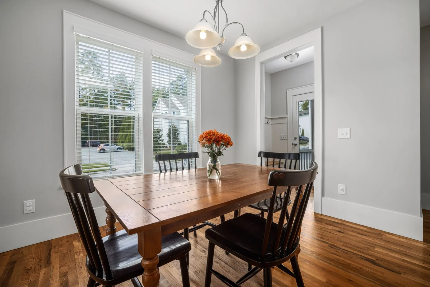 Bright dining room featuring a wooden table, chairs, flower vase, and modern ceiling lamp.