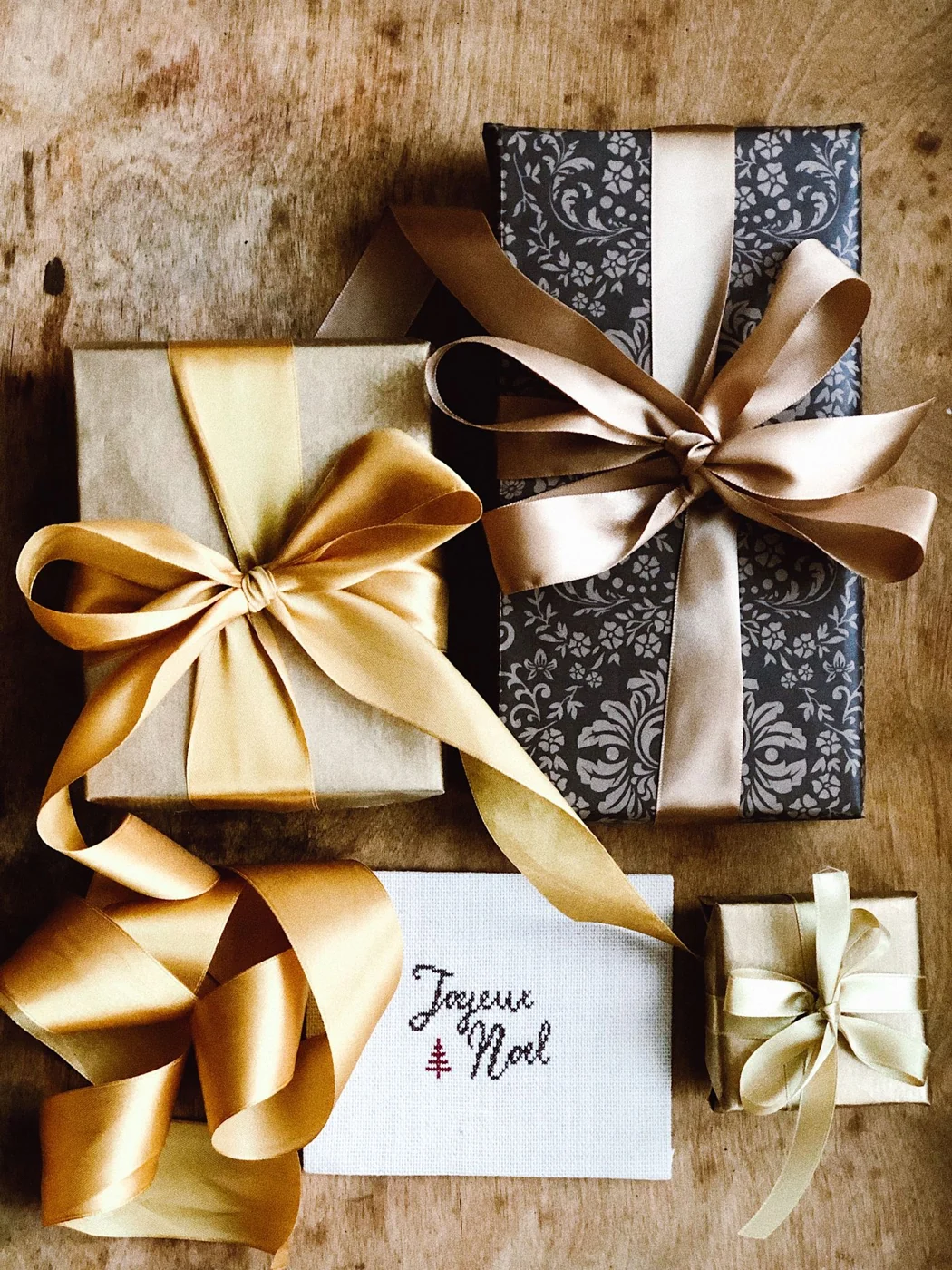 Beautifully wrapped gift boxes with ribbons and a "Joyeux Noël" card on a wooden surface.