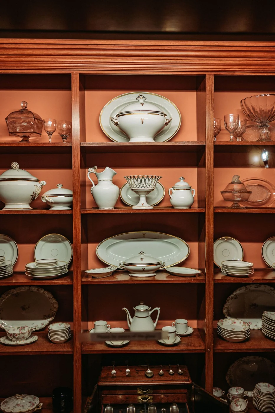 An elegant display of fine china and glassware in a wooden hutch.