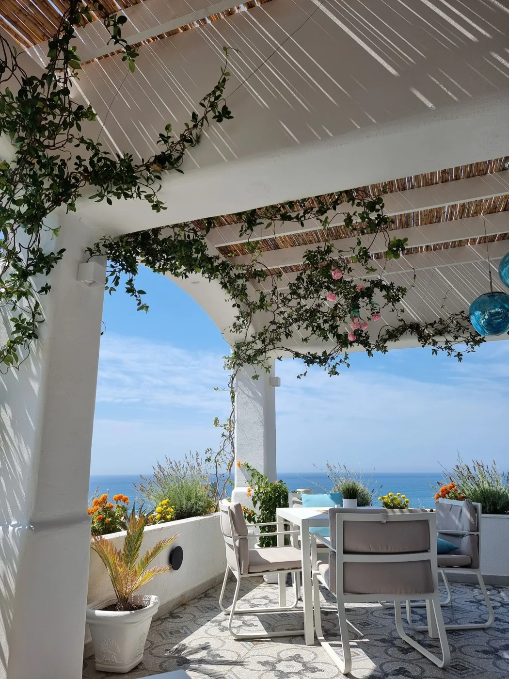 Charming seaside patio with chairs and table, offering stunning ocean views under a pergola.