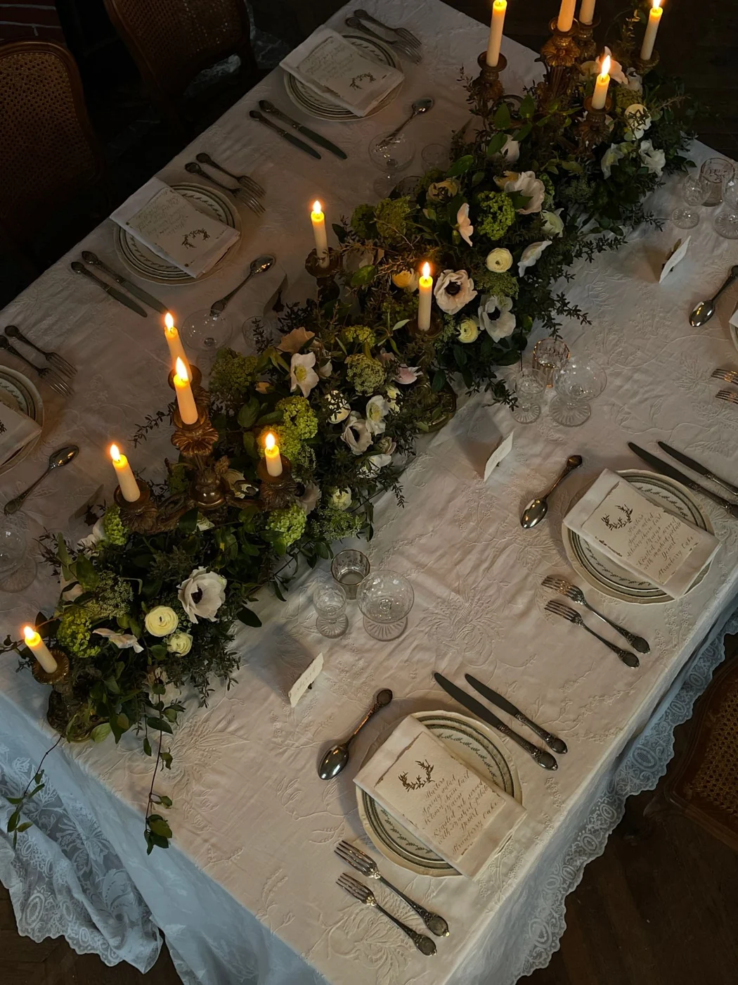 A low floral arrangement running along a table between individual place settings and candles.