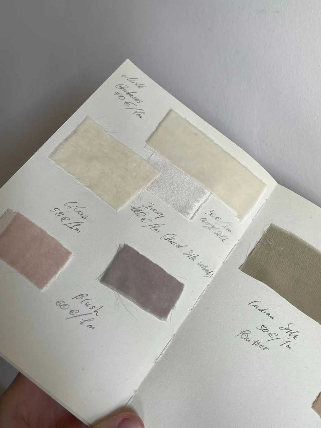 An open textile sample book showcasing various neutral fabric swatches labeled with textures and weights.