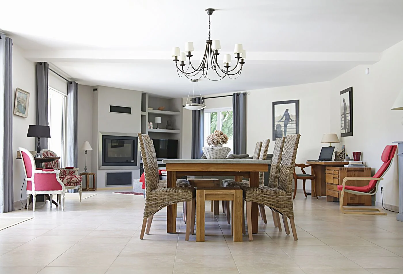 Spacious dining room with a chic chandelier, wicker chairs, wooden table, and cozy fireplace.