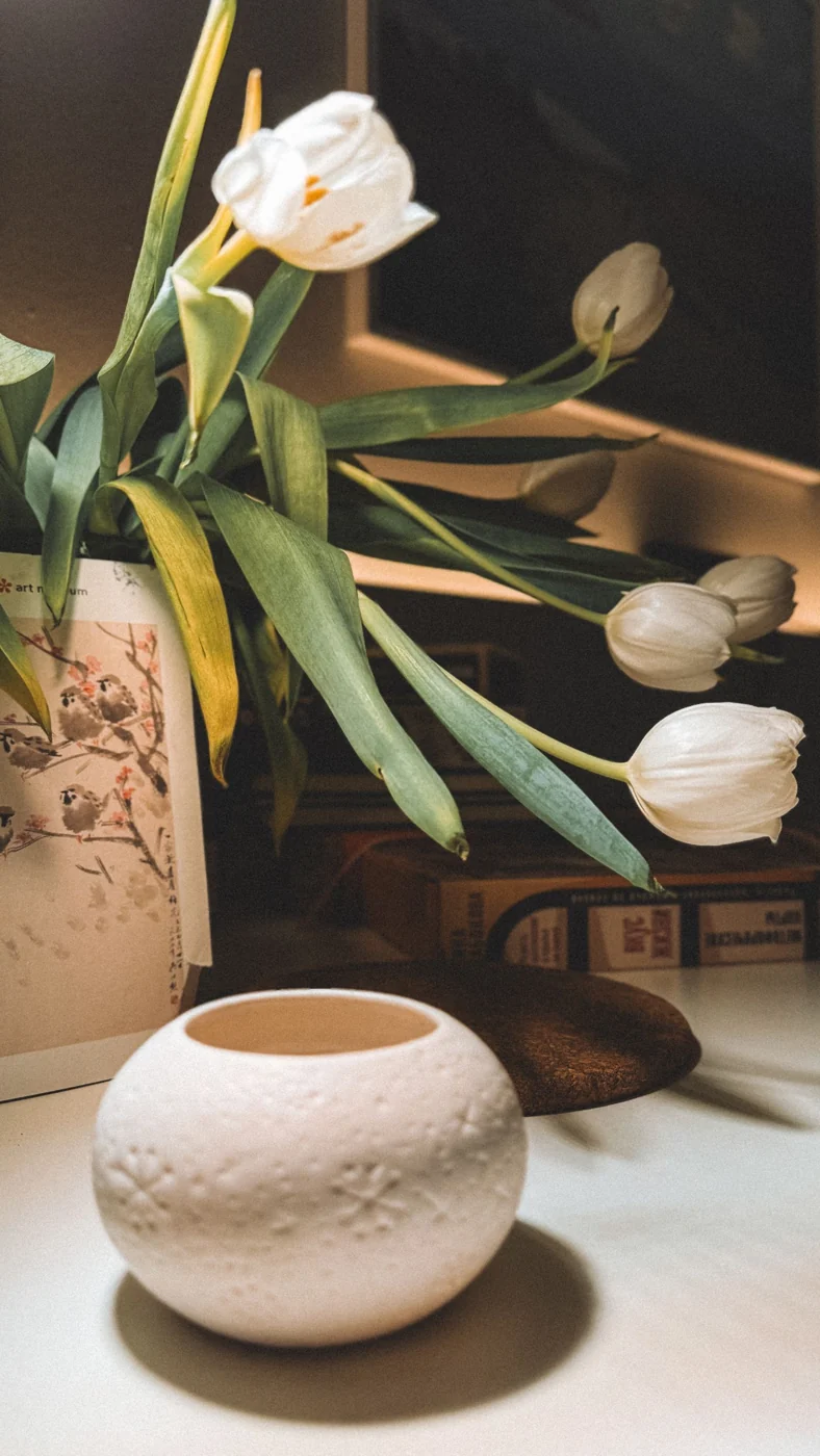 White tulips in an artistic vase on a table, creating a calm and elegant ambiance.