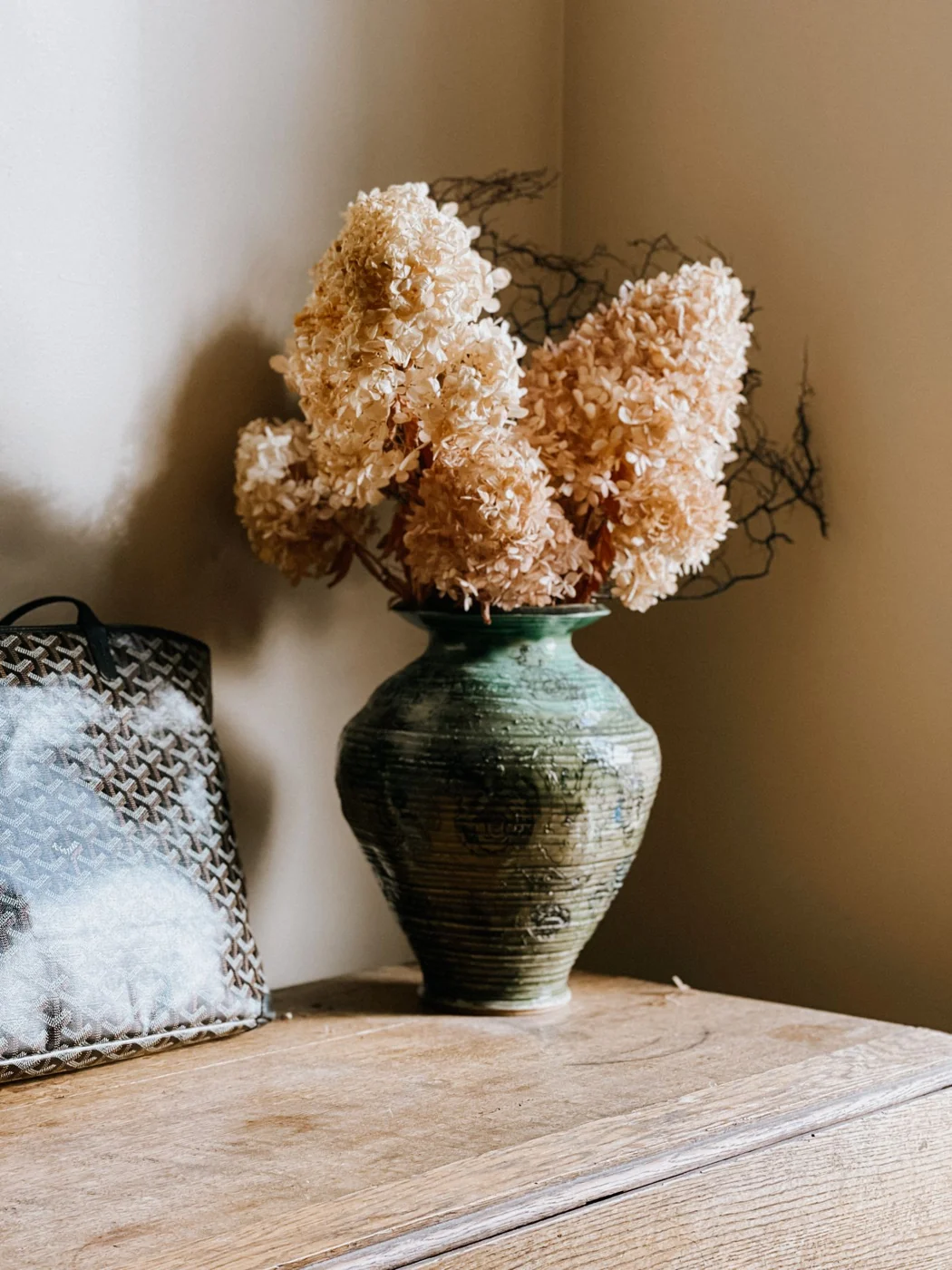 Artistic display of dried hydrangea flowers in a green vase, creating a warm, vintage aesthetic.