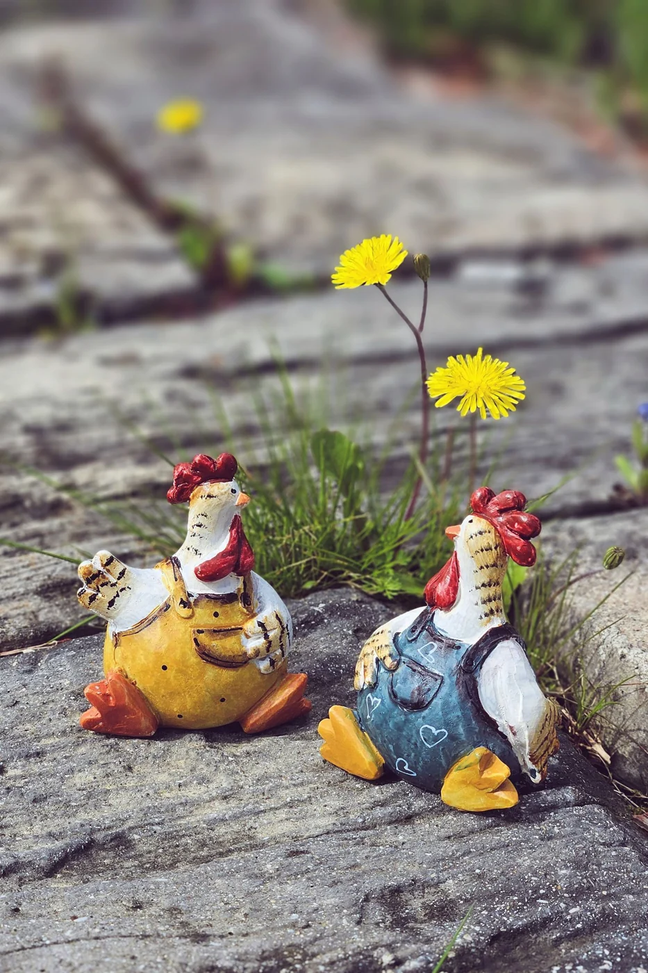 Small painted chicken ornaments on a stone garden path.