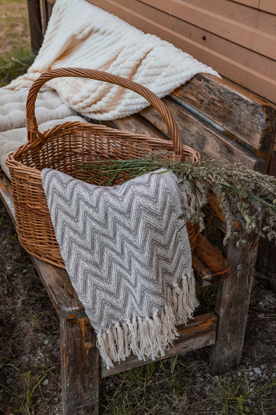 A rustic bench with a wicker basket, blanket, and decorative dried plants creates a cozy autumn vibe.