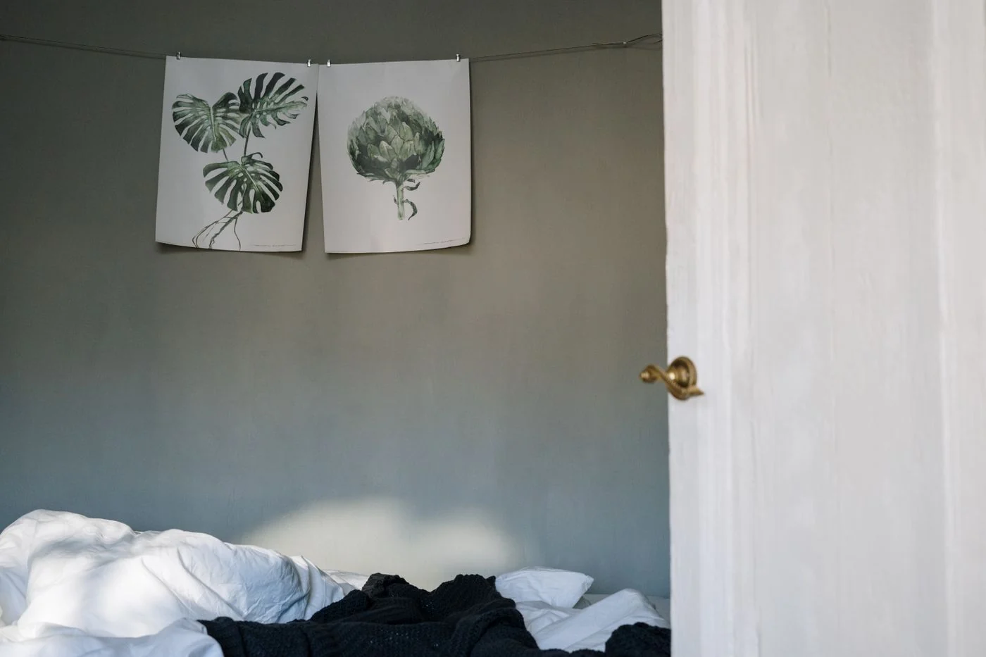 Botanical prints above a bed against a soft green wall.