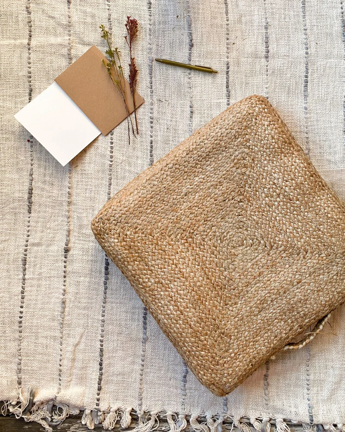 Handwoven cushion on a striped linen tablecloth with dried flowers and envelopes.