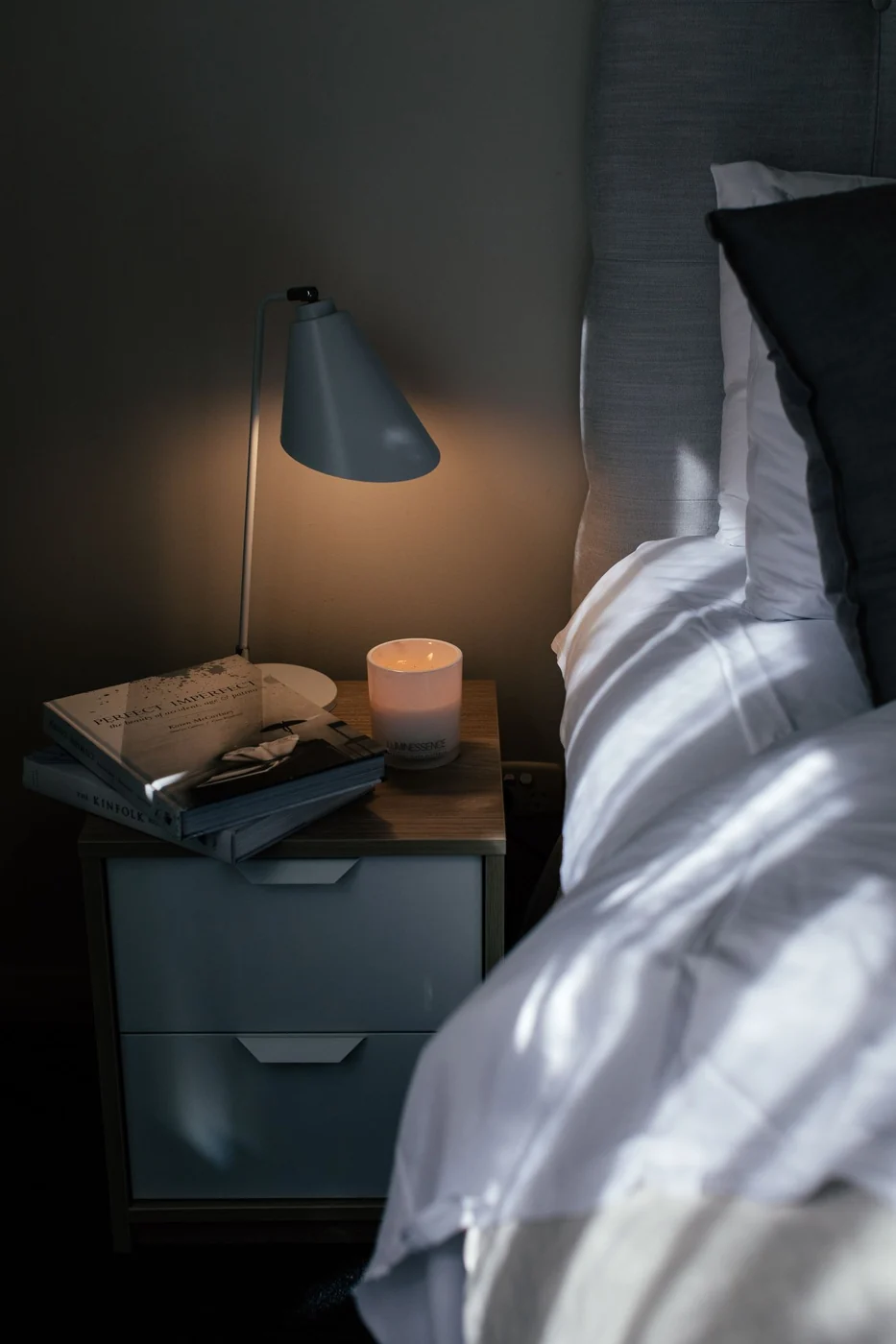 A serene bedroom scene with a lamp and books on a nightstand, creating a cozy ambiance.