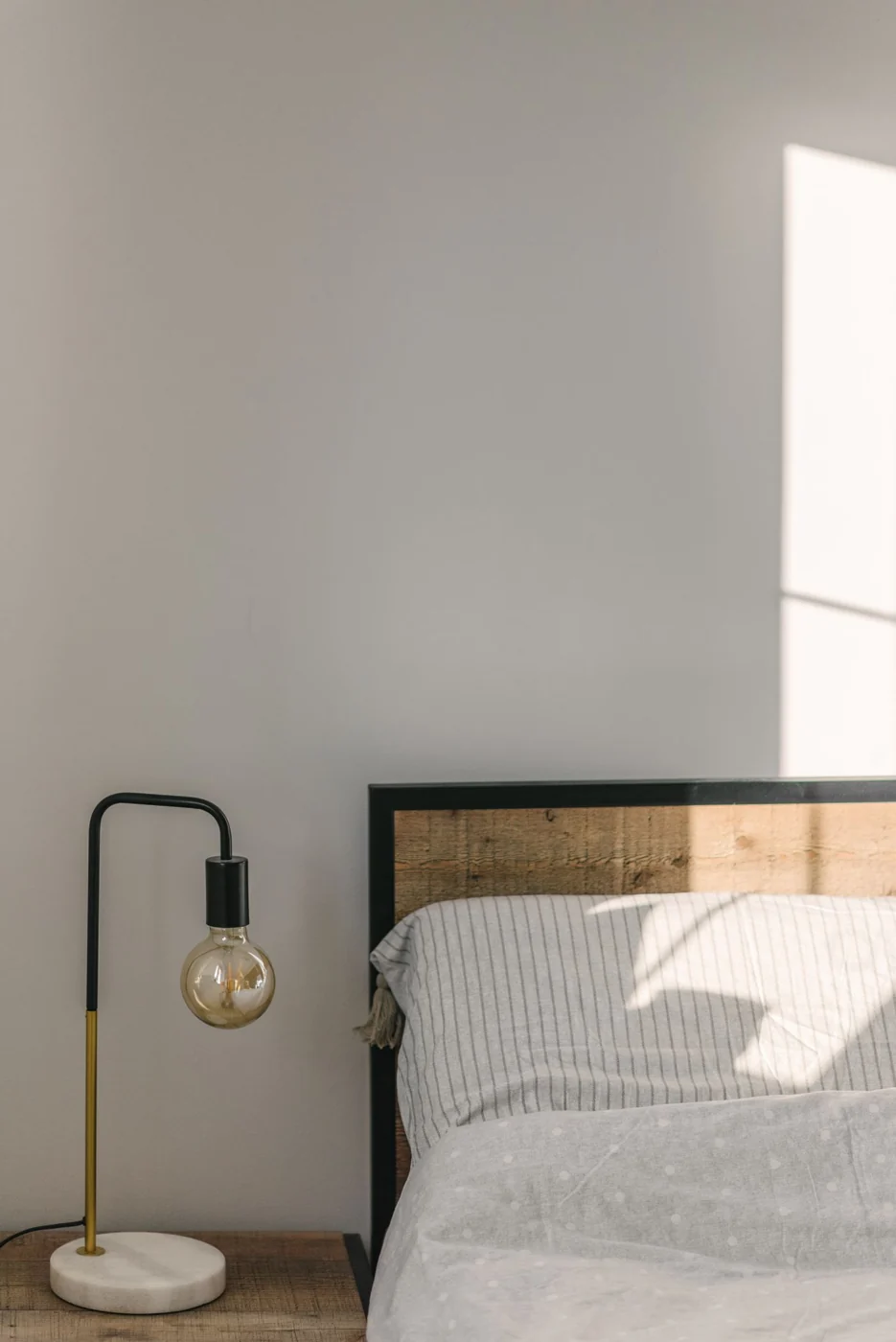 Cozy minimalist bedroom with wooden headboard and stylish lamp in natural light.