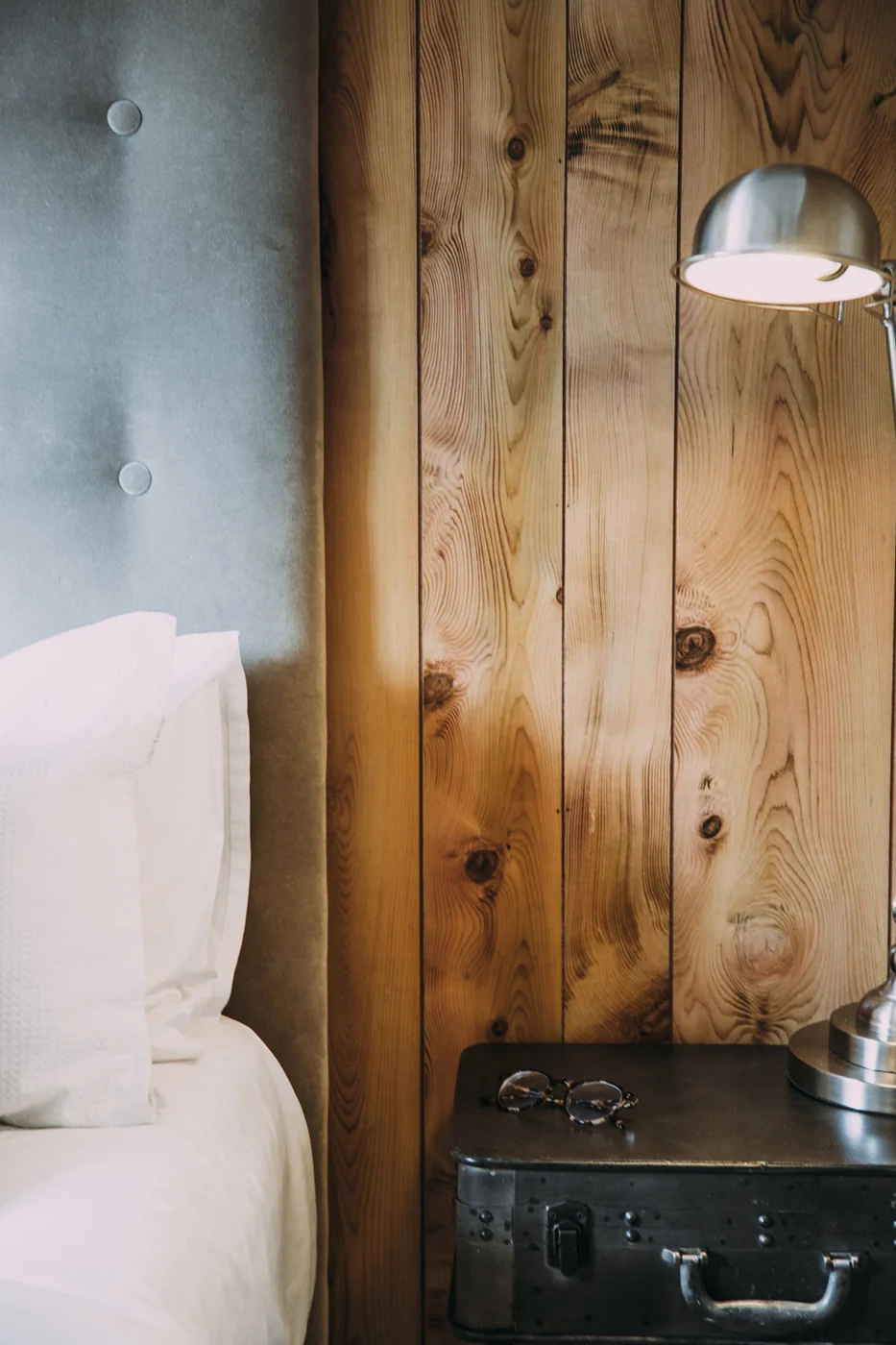 Elegant bedroom corner featuring a wooden wall, cozy bed, and metal lamp on an industrial nightstand.