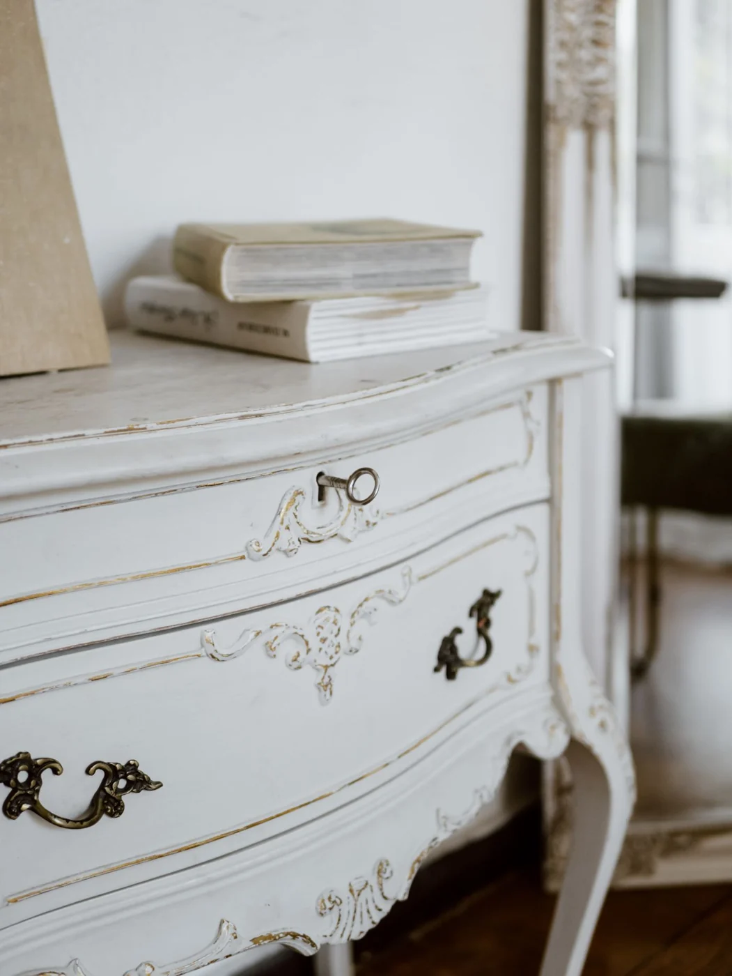 Close-up of an ornate vintage dresser with books and a key on top, enhancing a classic interior decor.