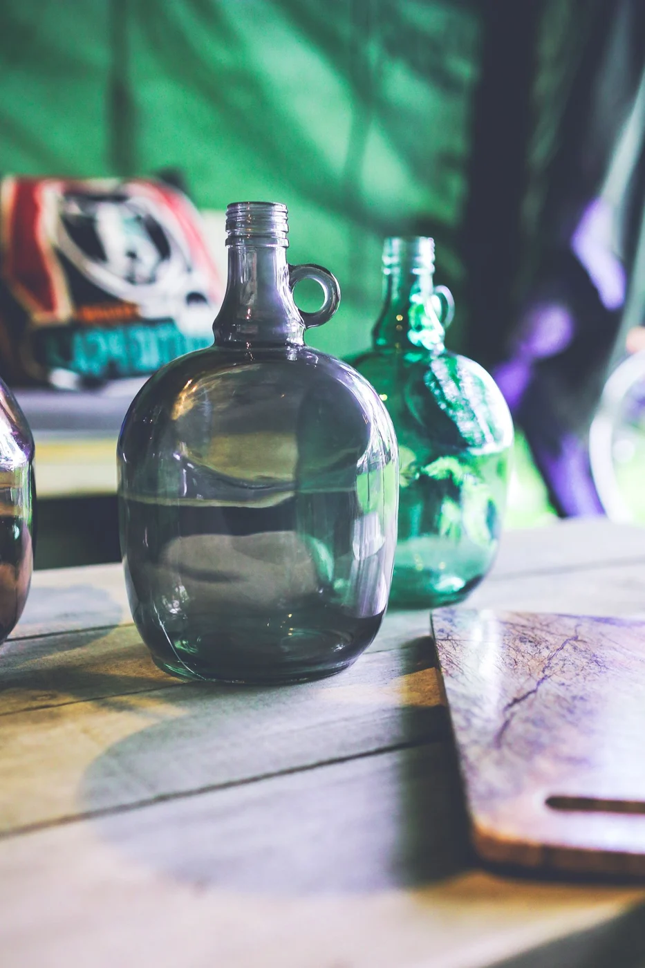 Large green glass bottle and smaller clear bottles on a wooden tabletop.