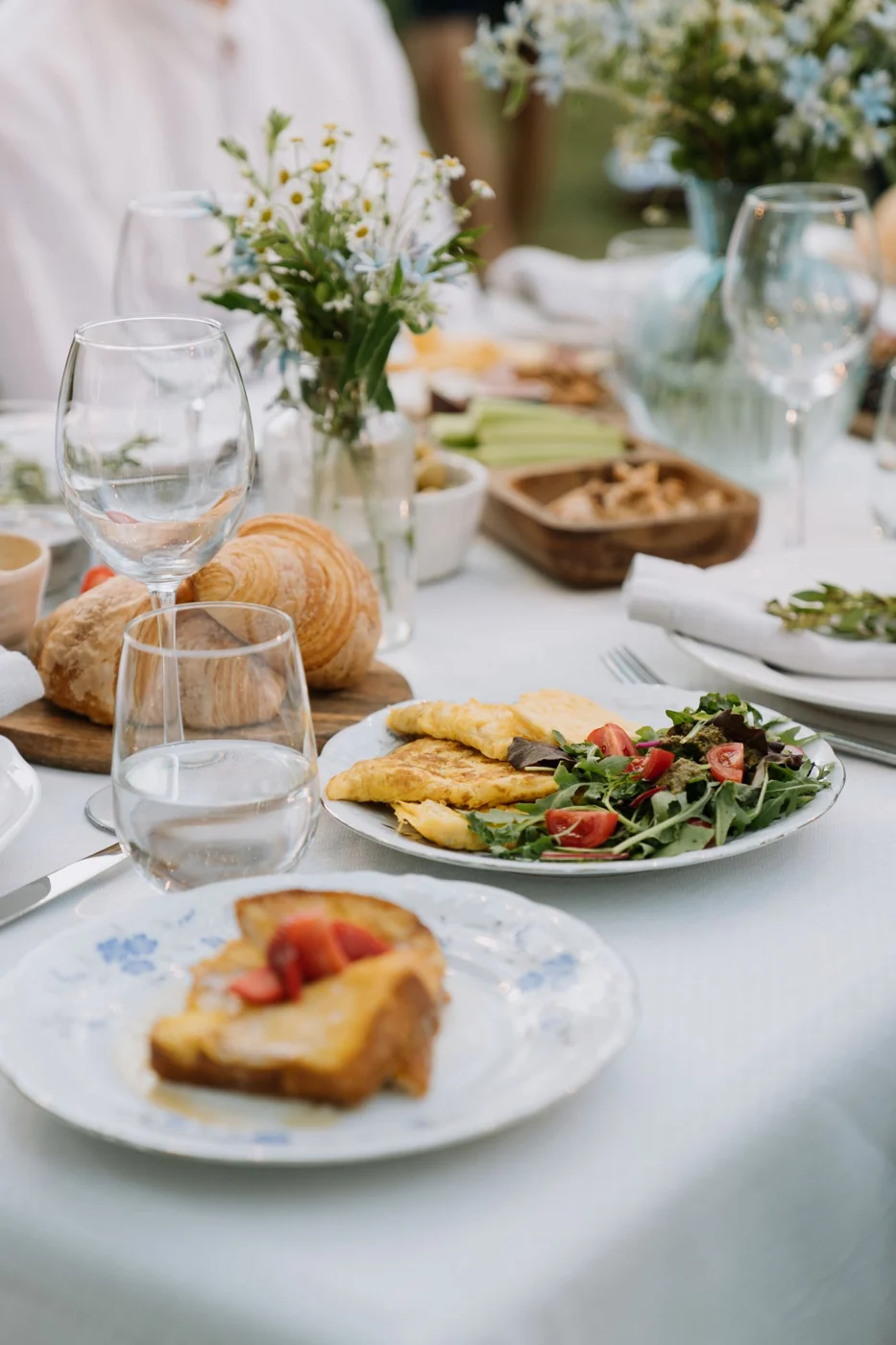 Cozy outdoor brunch setting with omelette and wine glasses on a floral tablecloth.
