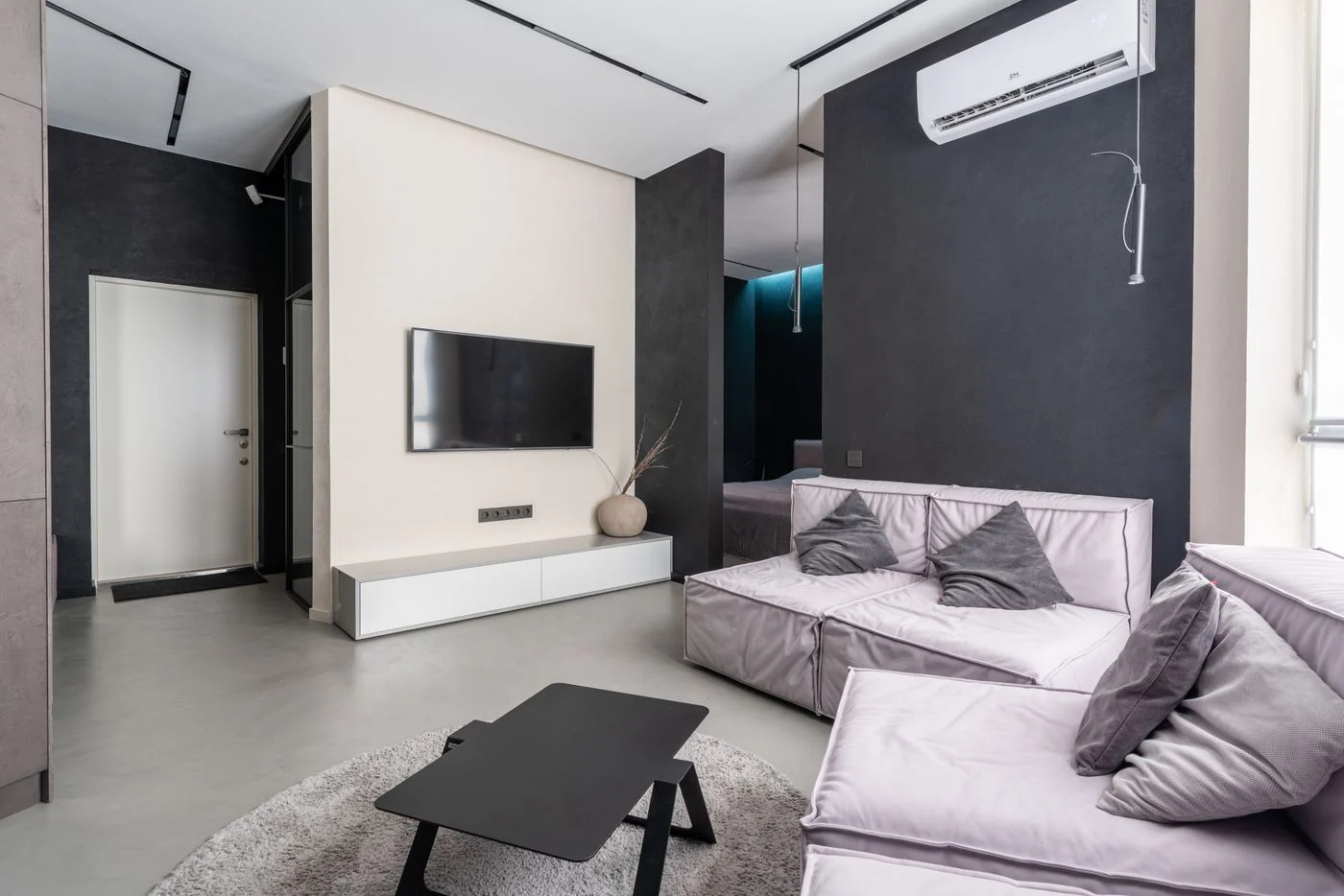 A living room with pale seating facing a television mounted on a white wall.