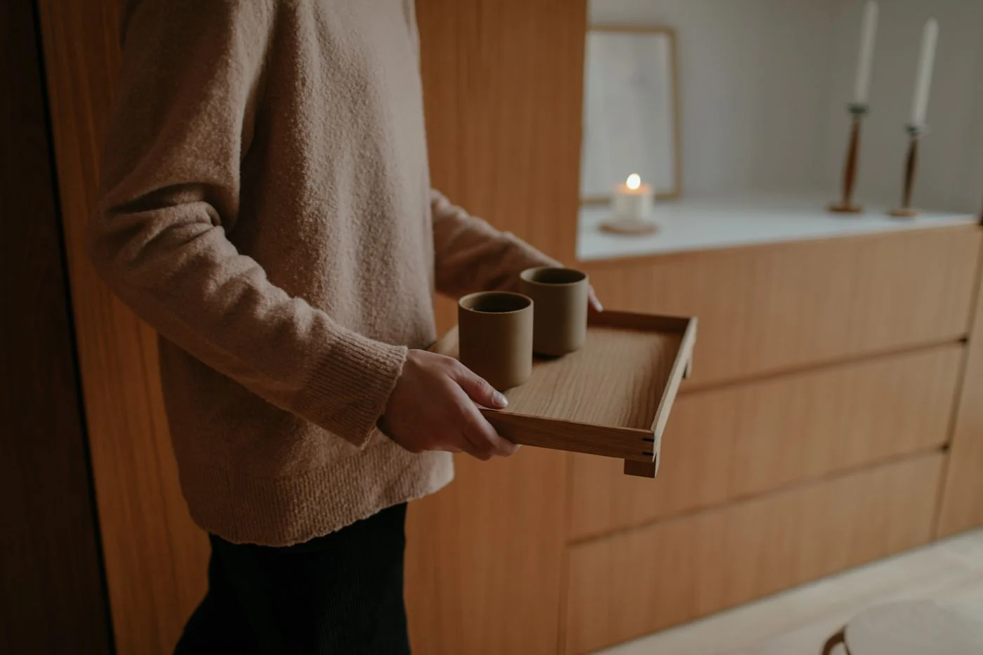 Warm indoor setting featuring a wooden tray with mugs and candlelight ambiance.