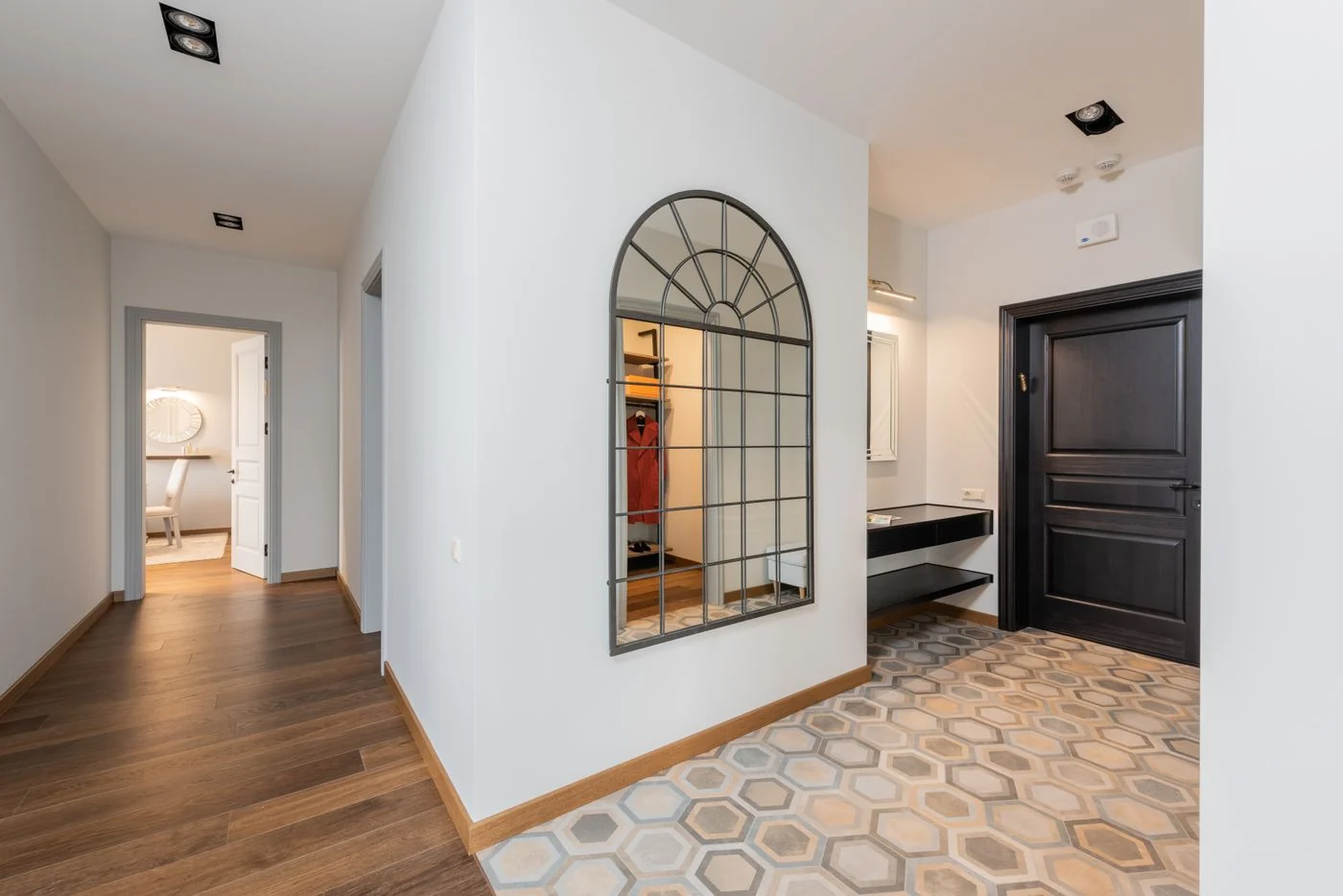 Bright, contemporary hallway featuring stylish mirror and dark wood door.