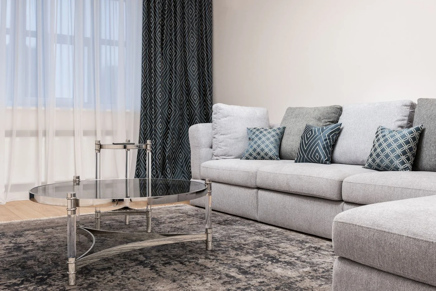Contemporary living room with gray sofa, round glass table, and geometric cushions.