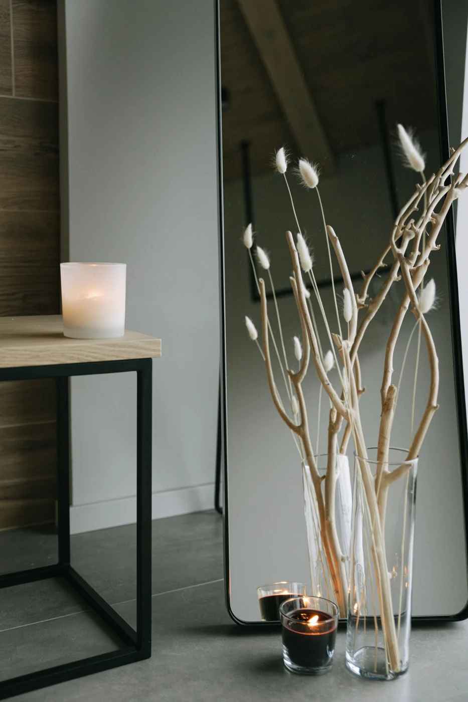 Bare branches in a tall clear glass vase beside a candle.