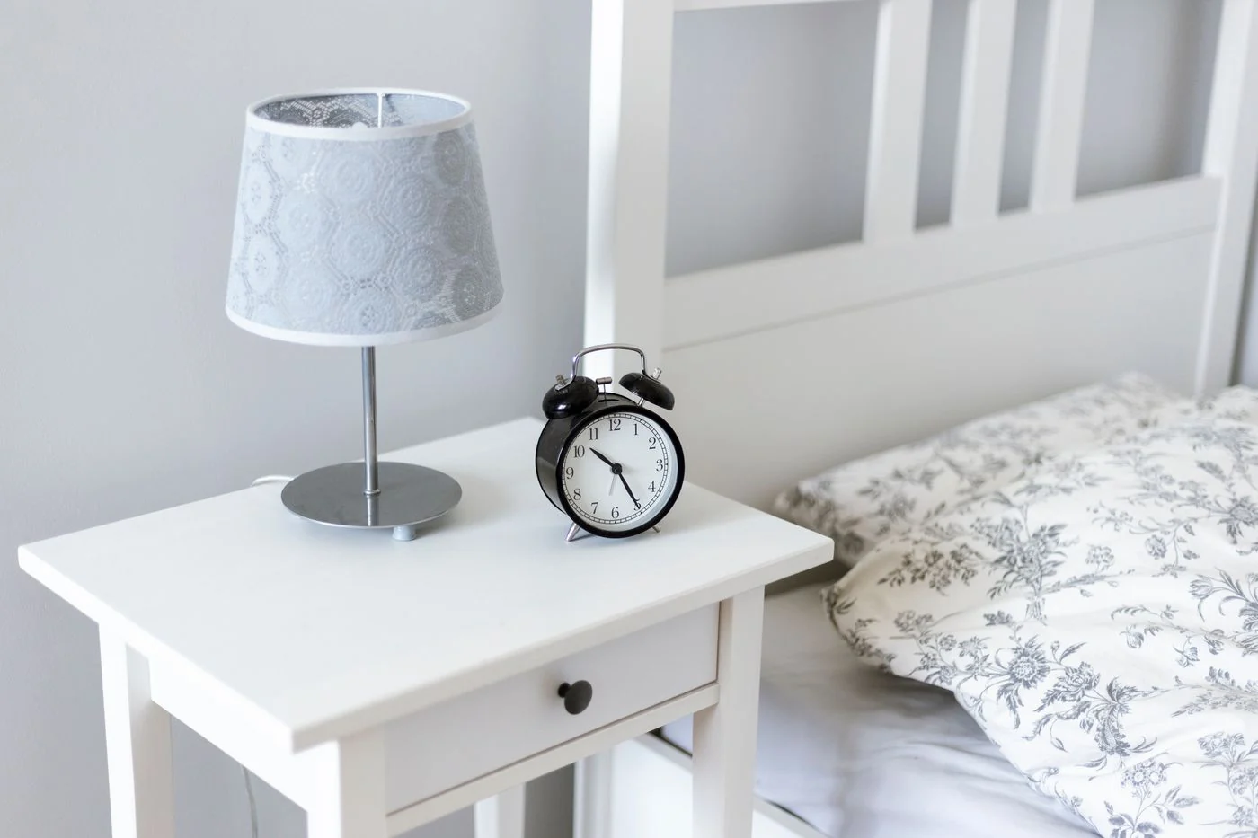 A simple and elegant bedroom setup with a bedside table, alarm clock, and lamp.