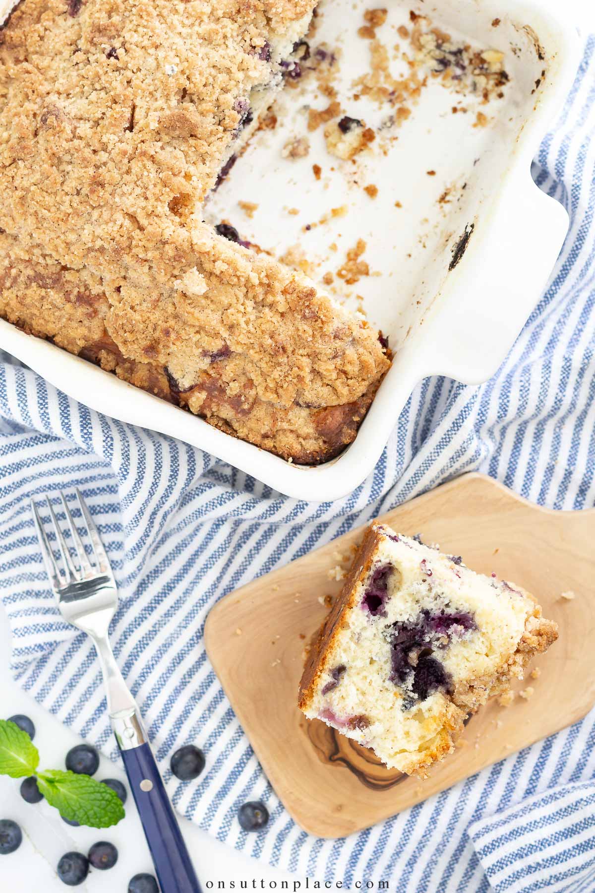 blueberry coffee cake in baking dish with piece on wood baord