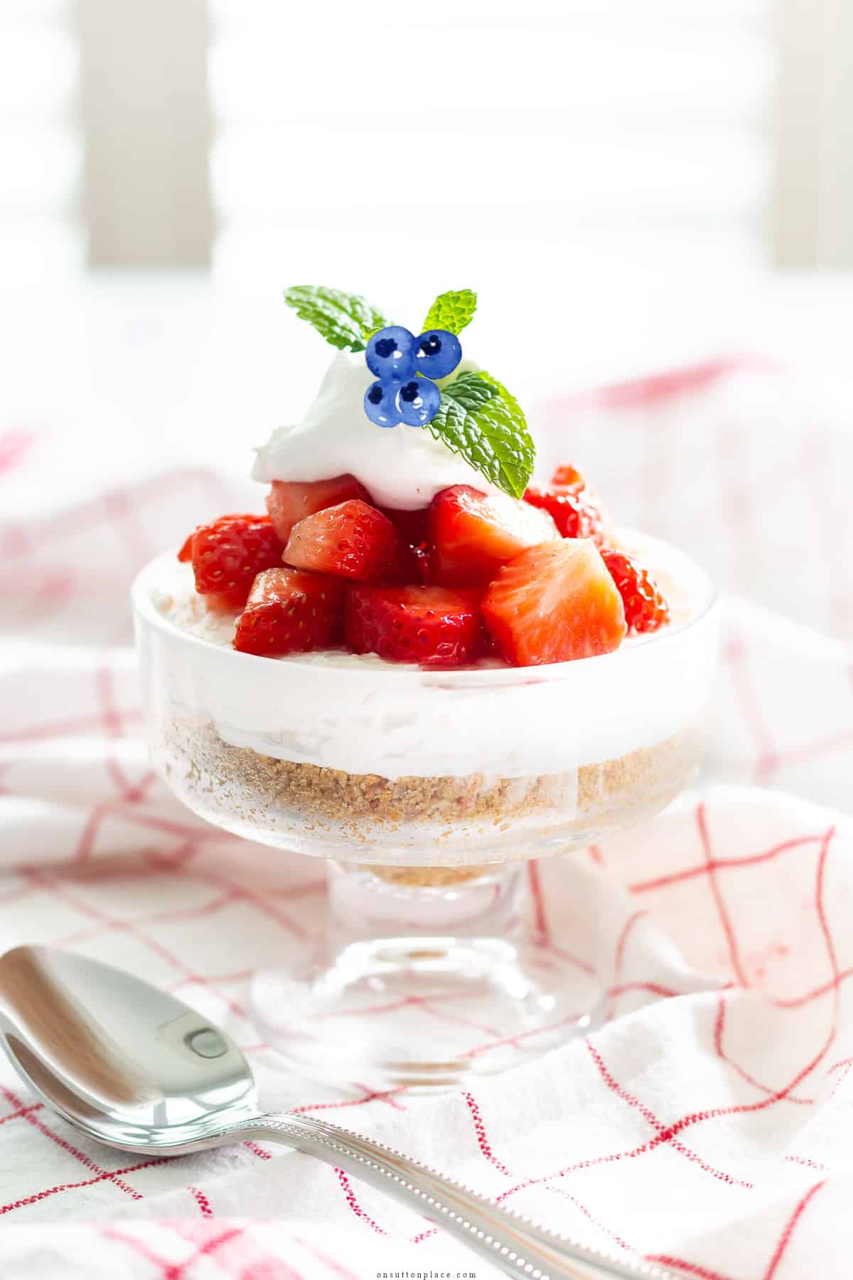 layered strawberry parfait recipe in clear dish with mint garnish and blueberries